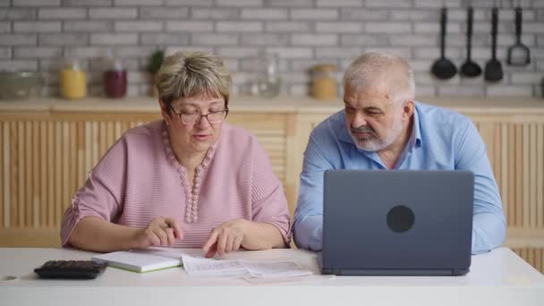 Casal idoso está calculando suas contas de serviços públicos sentados juntos na cozinha em casa, retrato médio — Vídeo de Stock