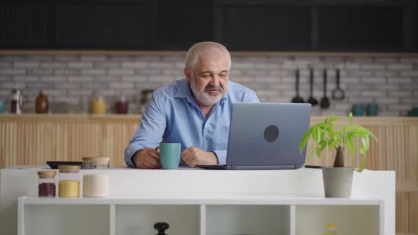 Anciano hombre está hablando por videollamada en el ordenador portátil con amigos o familiares, retrato de la persona en la cocina del hogar — Vídeos de Stock