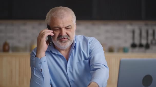 Orta yaşlı bir adam evden uzaktan çalışıyor, telefonla arıyor ve iş arkadaşı veya ortağıyla konuşuyor — Stok video