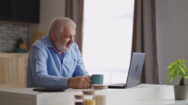 Orta yaşlı bir adam laptopta ailesiyle ya da arkadaşıyla görüntülü sohbet yapıyor. Evde tek başına oturuyor.