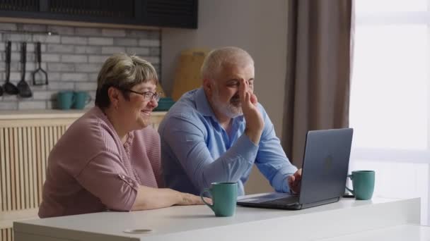 Vieux parents bavardent avec des enfants par ordinateur portable en utilisant un appel vidéo, homme âgé et femme sont assis à la cuisine, regardant la caméra web — Video