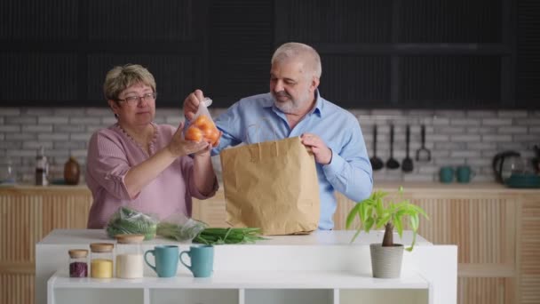 Бабушка и дедушка распаковывают покупки в продуктовом магазине или на рынке, свежие овощи и фрукты из супермаркета — стоковое видео