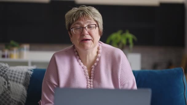 Mujer anciana se está comunicando por chat de vídeo en línea en el ordenador portátil con sus colegas o familiares, profesor está dando conferencias en línea, modo de trabajo distante — Vídeos de Stock