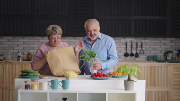 Las personas mayores están desempacando alimentos después de comprar en el supermercado o el mercado, tomando verduras frescas de la bolsa de papel ecológico — Vídeos de Stock