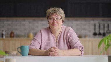 Büyükannem mutfakta oturuyor ve kameraya bakıyor, dinliyor ve kafa sallıyor, online görüntülü sohbet konsepti.
