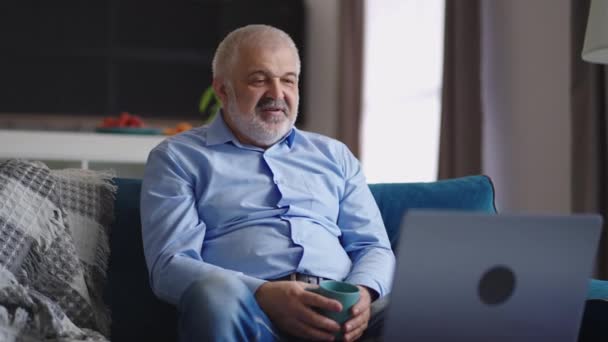 Viejo hombre está trabajando de forma remota desde casa, charlando por chat de vídeo en línea en el ordenador portátil con colegas o socios, el modo de trabajo distante — Vídeos de Stock