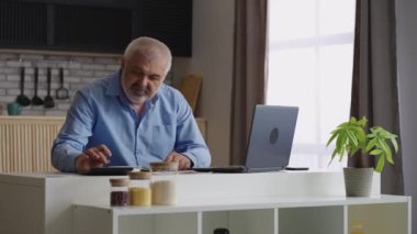 Gri saçlı adam ev ofisinde çalışıyor, hesap yapıyor ve rapor hazırlıyor, mali direktör ya da denetçi.