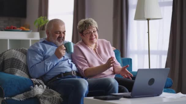 Зріла людина і жінка сидять на дивані і спілкуються за допомогою відеодзвінка в ноутбуці з сім'єю, відпочиваючи на вихідних вдома — стокове відео