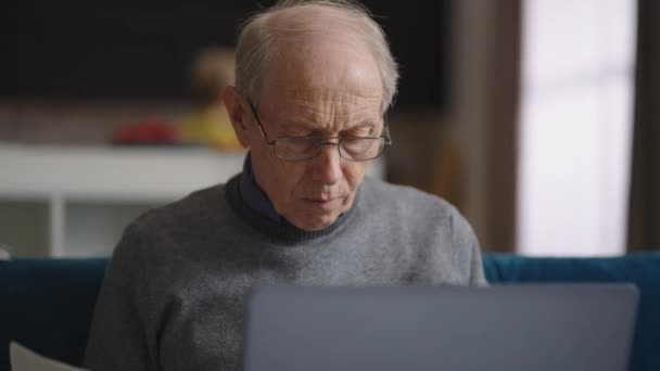Γέρος ρυτιδιασμένος και φαλακρός άνθρωπος εργάζεται στο γραφείο του στο σπίτι, πορτρέτο του ανδρός συνταξιούχος στο διαμέρισμα, χρησιμοποιώντας φορητό υπολογιστή για την εργασία — Αρχείο Βίντεο