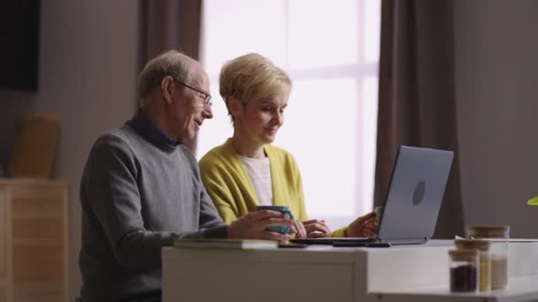 Shopping online da casa, vecchio e donna stanno visualizzando le merci sul sito del negozio internet seduto in cucina — Video Stock