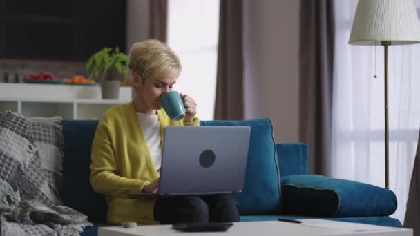 Gammal dam kommunicerar i sociala nät, använder laptop för att skicka meddelanden, vila ensam hemma på helgen — Stockvideo