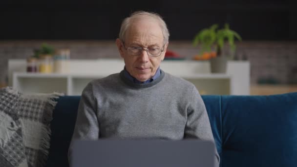 Homme âgé se repose dans son appartement le week-end, la personne âgée utilise un ordinateur portable pour discuter par appel vidéo avec un ami ou une famille — Video