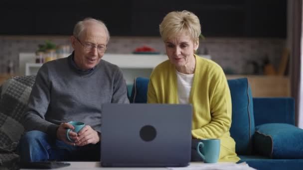 Yaşlı evli çift laptopta arkadaşlarıyla ya da aileleriyle görüntülü sohbet yaparak hafta sonları evde dinleniyor. — Stok video