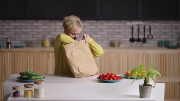 Mujer jubilada está desempacando bolsa con comida del servicio de entrega, poniendo productos en la mesa de la cocina, retrato femenino — Vídeo de stock