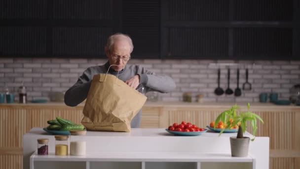 退休人员正在打开装有送货服务食品的袋子，把货物放在厨房桌子上 — 图库视频影像