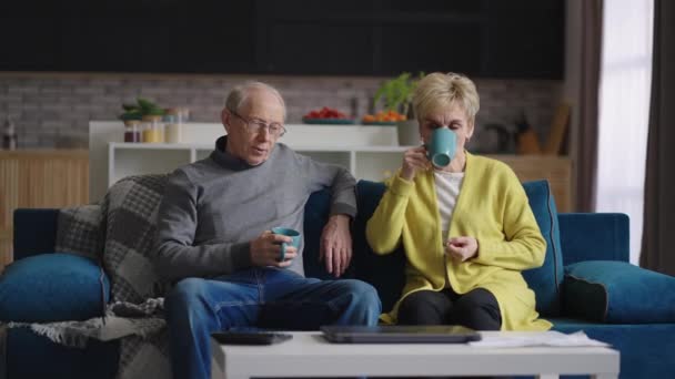 Calme couple marié de personnes âgées se repose à la maison le week-end, mamie et grand-père boivent du thé dans le salon de l'appartement — Video