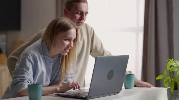 Pareja 30 esposa y marido en la cocina utilizando el ordenador portátil disfrutar de e-shopping de forma remota, la planificación de la reubicación futura elegir servicios de la firma de renovación en línea. Comercio electrónico actividad fácil y confortable desde el concepto de hogar — Vídeos de Stock