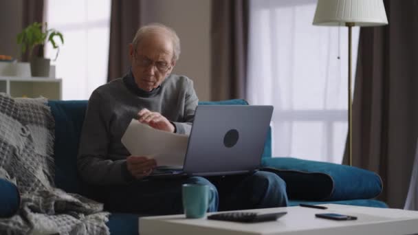 starší muž kontroluje účty za elektřinu a používá notebook doma, důchodce počítá své výdaje