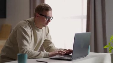 Gözlüklü bir adam evinde bilgisayarla ve internetle çalışıyor. Uzak çalışma ve uzak öğrenim