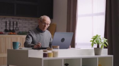 Emekli adam evden uzaktan çalışıyor, hesap makinesiyle sayıyor ve laptopunu dolduruyor, deneyimli muhasebeci