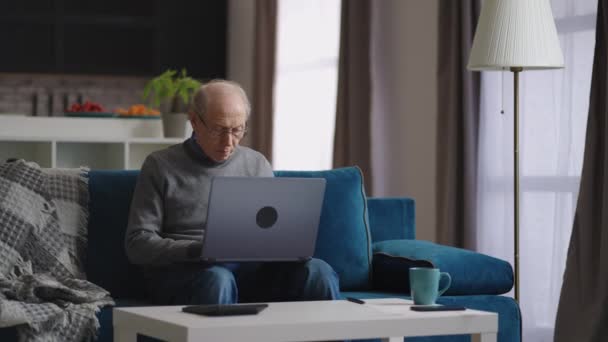 Ensam gammal man sitter hemma och arbetar med laptop, porträtt av pensionär i vardagsrummet i sin lägenhet — Stockvideo
