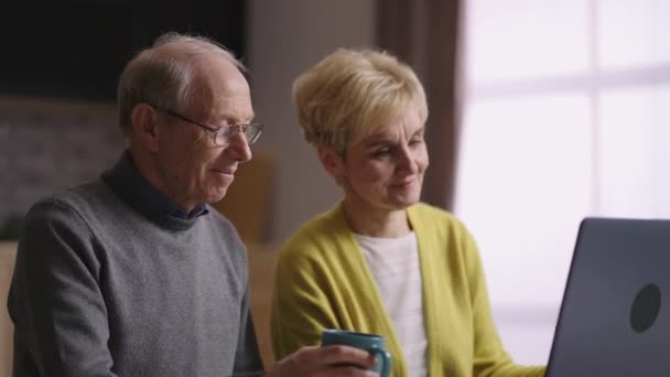 Yaşlı evli çift, dizüstü bilgisayardaki görüntülü sohbet yoluyla arkadaşlarıyla iletişim kuruyor, web kamerasına gülümsüyor, portre — Stok video