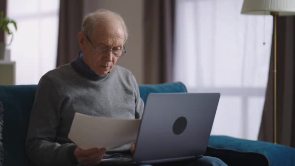 Viejo hombre está trabajando con el papel y el ordenador portátil en el hogar, anciano está llenando formulario en el sitio de Internet, el pago de facturas en línea — Vídeos de Stock