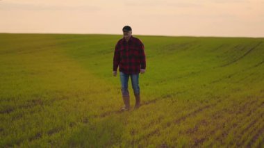 Yaşlı bir çiftçi çizmeleriyle tarlada yürüyor ve kamera onu izliyor.