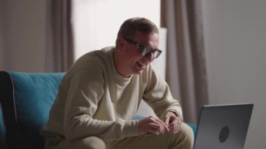 Evdeki koltukta oturan adam kendini izole etmek için dizüstü bilgisayarla video çekiyor. Evde çalışan, dizüstü bilgisayarlı video konferansında konuşan mutlu sarışın öğretmen..