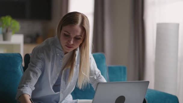 Ernstige jonge vrouw freelancer werken aan freelance van thuis uit typen e-mail op laptop, gericht meisje met behulp van computer voor studie online thuis zitten op de bank, vrouwelijke gebruiker bezig op afstand internet baan — Stockvideo