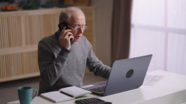 Yaşlı adam koronavirüs salgını sırasında uzaktan çalışıyor, yaşlı adam dizüstü bilgisayar kullanıyor ve telefonla arıyor.