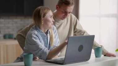 30 'lu yaşlardaki karı koca dizüstü bilgisayarlarıyla mutfaktan e-alışveriş yapıyor, gelecekte taşınmayı planlıyor ve yenileme firmalarını online olarak seçiyor. E-ticaret kolay ve konfor aktivitesi ev kavramından