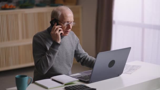 Idős férfi távolról dolgozik otthonról a koronavírus világjárvány idején, idős ember laptopot használ és telefonál — Stock videók