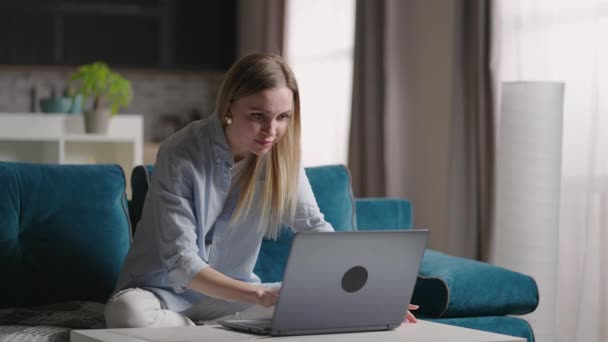 Ciddi genç kadın serbest çalışan, bilgisayarında e-posta yazan, evde bilgisayar kullanan, kanepede oturan, uzak internet işiyle meşgul bir kadın. — Stok video