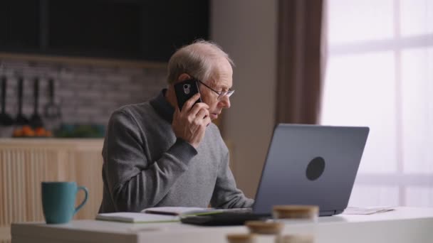 Jubilado hombre está trabajando a distancia en la oficina en el hogar, anciano está llamando por teléfono para comunicarse con colegas o socios — Vídeos de Stock