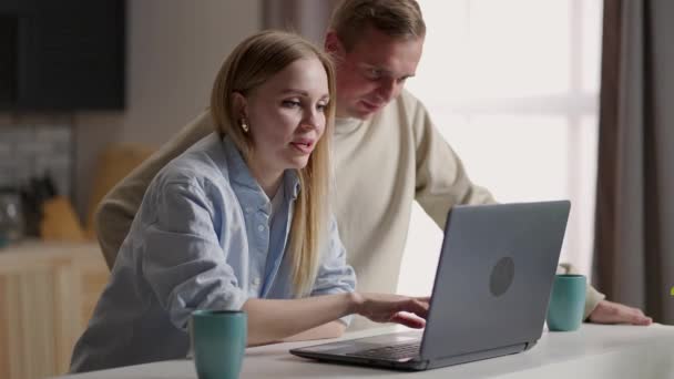 Bonding millennial sonriente pareja mirando a la pantalla del ordenador portátil, la elección de los productos en la tienda en línea que participan en las compras por Internet, discutir la planificación de viajes de vacaciones reserva de hotel o billetes de avión en el ordenador — Vídeo de stock