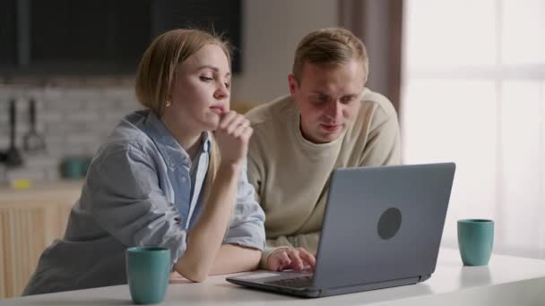 Unga par tillbringar helgen hemma i köket med hjälp av laptop websurfing, diskutera inköp göra ordning mat på nätet, njuta av enkel komfort köpa på e-handel tjänster, söka renovering idéer internet — Stockvideo