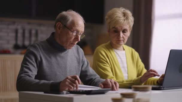 Elderly married spouses are counting family budget, sitting at home kitchen, calculating for save money — Stock Video