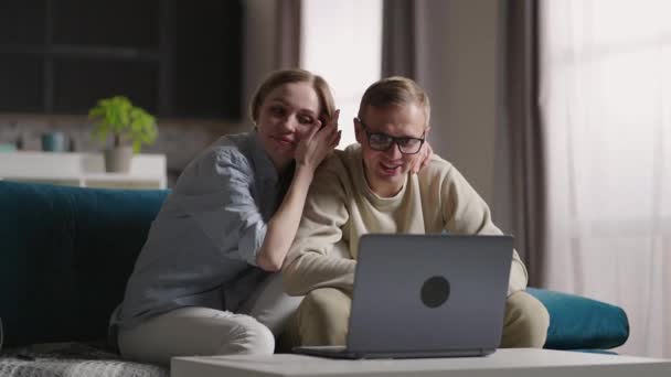 Νεαρό χαριτωμένο παντρεμένο ζευγάρι μαζί κουβεντιάζοντας σε βίντεο κλήση στο διαδίκτυο στο φορητό υπολογιστή κάθεται σε καναπέ στο νέο διαμέρισμα. Έννοια μετεγκατάστασης — Αρχείο Βίντεο