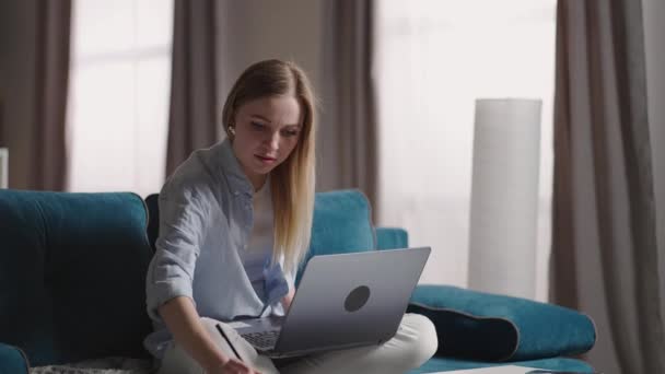 Allvarlig ung kvinna frilansare som arbetar på frilans från hemmet skriva e-post på laptop, fokuserad flicka med hjälp av dator för studier online hemma sitter på soffan, kvinnlig användare upptagen på distans internet jobb — Stockvideo