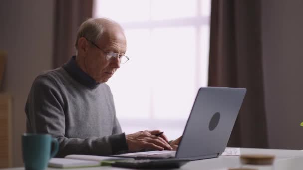 Äldre man lär sig online hemma, självstudier av pensionär, gammal man använder laptop, letar efter information på internet — Stockvideo