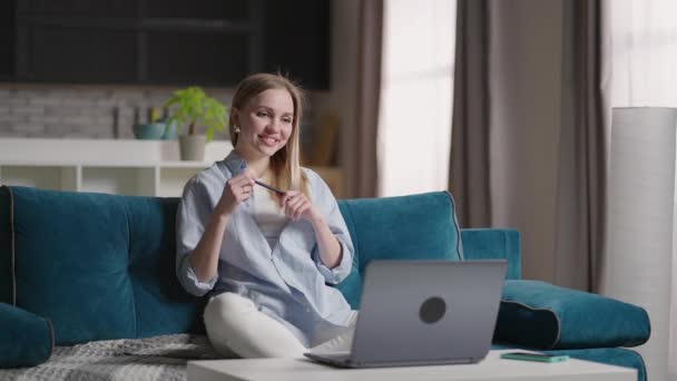 Femme assise sur le canapé à la maison faisant appel à la vidéo en utilisant un ordinateur portable sur l'isolement personnel. Joyeux jeune professeur blonde femme travaillant de la maison, parler sur ordinateur portable vidéoconférence. — Video