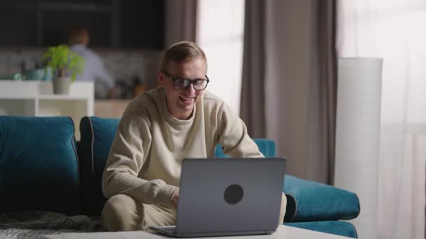 Man sitter på soffan hemma gör videosamtal Använda bärbar dator på själv isolering. Glad ung blond lärare man som arbetar hemifrån, talar på laptop videokonferens. — Stockvideo