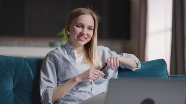 Frau, die zu Hause auf dem Sofa sitzt und Videotelefonate mit dem Laptop führt. Glückliche junge blonde Lehrerin arbeitet von zu Hause aus und spricht auf einer Laptop-Videokonferenz. — Stockvideo