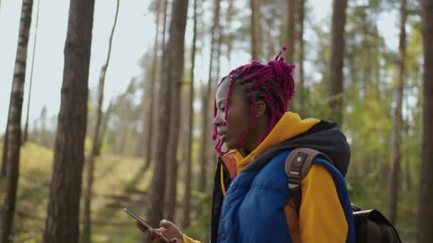 带背包的黑人妇女使用智能手机Gps 。非洲裔美国女孩在森林中远足，在智能手机上打字。单身女性徒步旅行者使用森林智能手机. — 图库视频影像