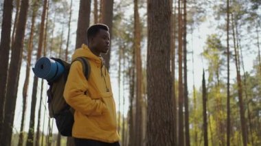 Afrikalı siyahi adam, sırtında ağır çekimde sırt çantasıyla ormanda yokuş yukarı tırmanıyor.