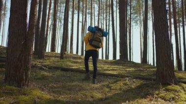 Afrikalı siyahi adam, sırtında ağır çekimde sırt çantasıyla ormanda yokuş yukarı tırmanıyor.