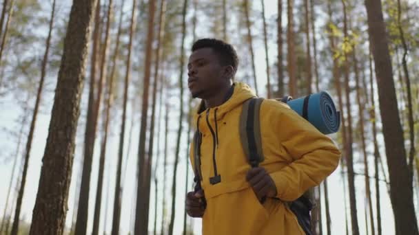 Uomo nero africano sale in salita nel bosco in giacca gialla con zaino al rallentatore — Video Stock