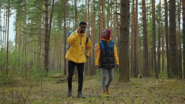 Twee Afrikaans-Amerikaanse reizende wandelaars met rugzak wandelen terwijl ze het landschap in het bos bekijken. Paar zwarte mannen en vrouwen op reis met de mobiele telefoon op ontdekkingstocht door wilde bossen natuur in team — Stockvideo