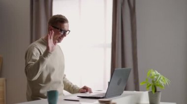 Gülümseyen genç erkek canlı yayında bilgisayar ve video konferans kullanarak iletişim kuruyor. Genç erkek video bağlantısıyla iletişim kurarken not alıyor